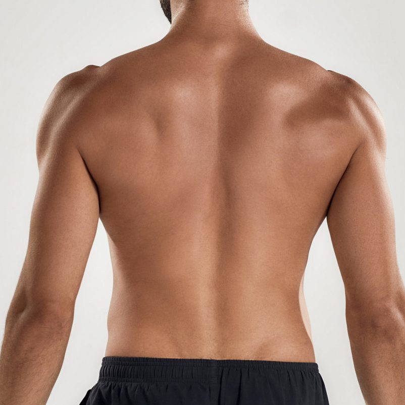 Rear view of muscular man with naked posing isolated over grey background, studio shot. Sports, workout, bodybuilding